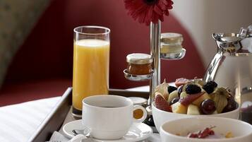 Bandeja de desayuno con un vaso de jugo de naranja, un tazón de fruta, una taza, un tarro de miel y una cafetera.