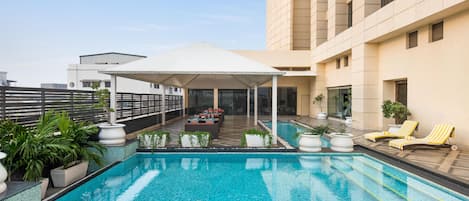 A rooftop pool with a covered seating area, potted plants, and lounge chairs.