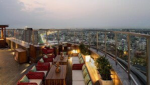 A rooftop terrace with seating areas, a city view, and a glass railing. - Hilton Jaipur (Jaipur)