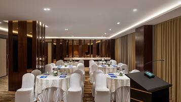 A conference room with round tables, white chairs, a podium, and a long table with a buffet setup.