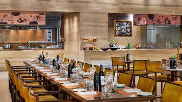 A restaurant with long wooden tables, chairs, and a bar area.