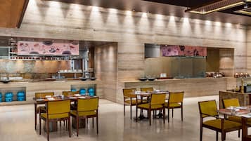 A restaurant with wooden walls, tables with yellow chairs, and a kitchen area with pots and pans.