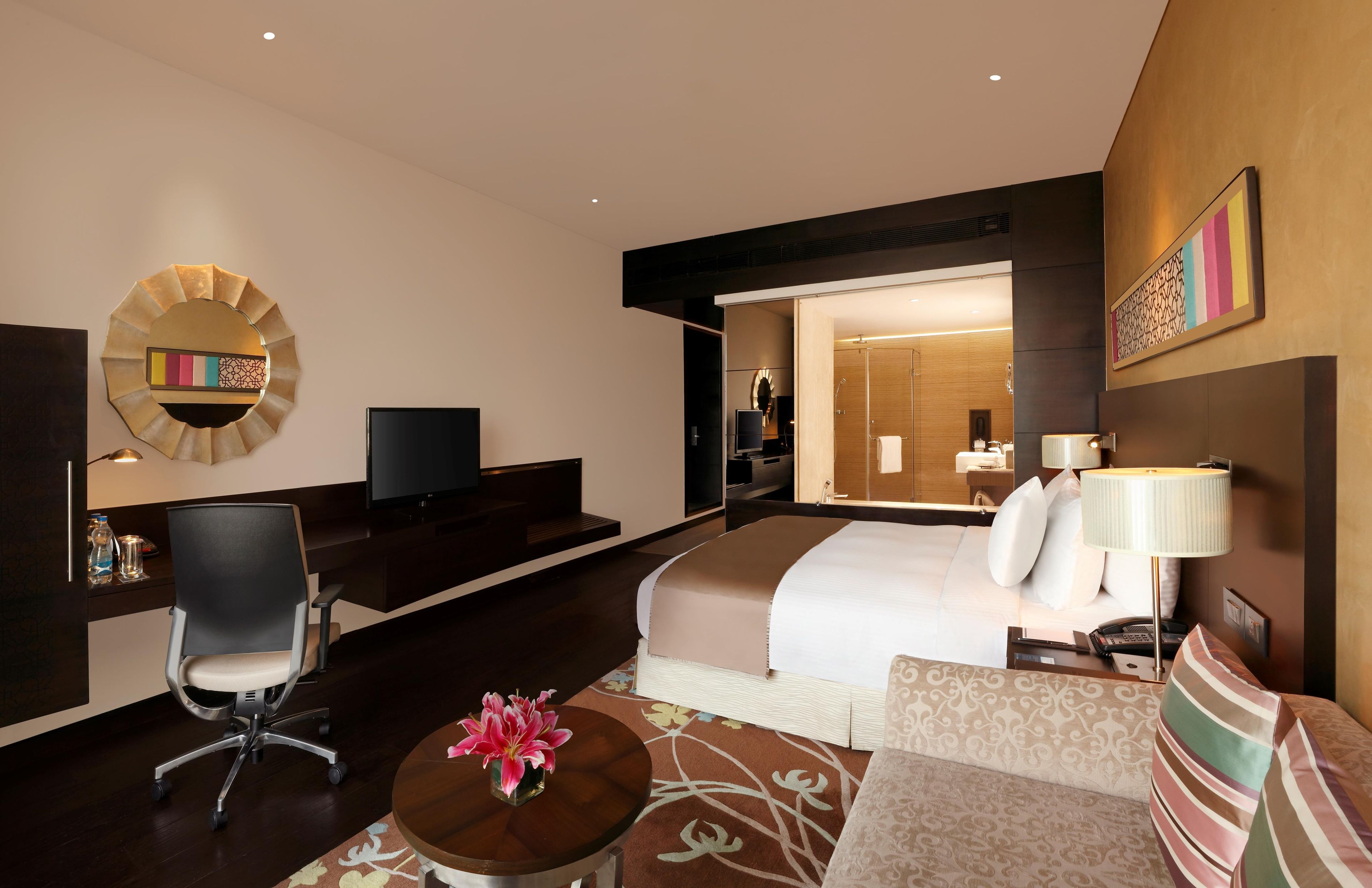 A hotel room with a bed, a desk, a chair, a TV, and a bathroom visible through an open door.