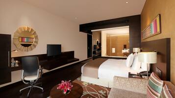 A hotel room with a bed, a desk, a chair, a TV, and a bathroom visible through an open door.