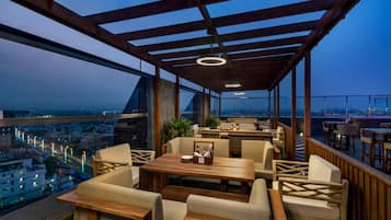 A rooftop terrace with seating, a wooden table, and a city view.