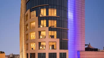 Een hoog, modern hotel met een gebogen gevel, verlichte signage en een goed verlichte entree.