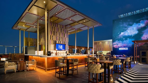 A rooftop bar with a bar counter, seating, and a large screen displaying a cosmic scene. - Hilton Jaipur (Jaipur)