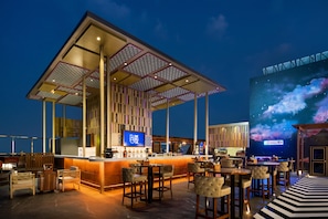 A rooftop bar with a bar counter, seating, and a large screen displaying a cosmic scene. - Hilton Jaipur (Jaipur)