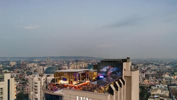 Um hotel com bar no terraço, fachada de vidro ampla e vista para a paisagem urbana.