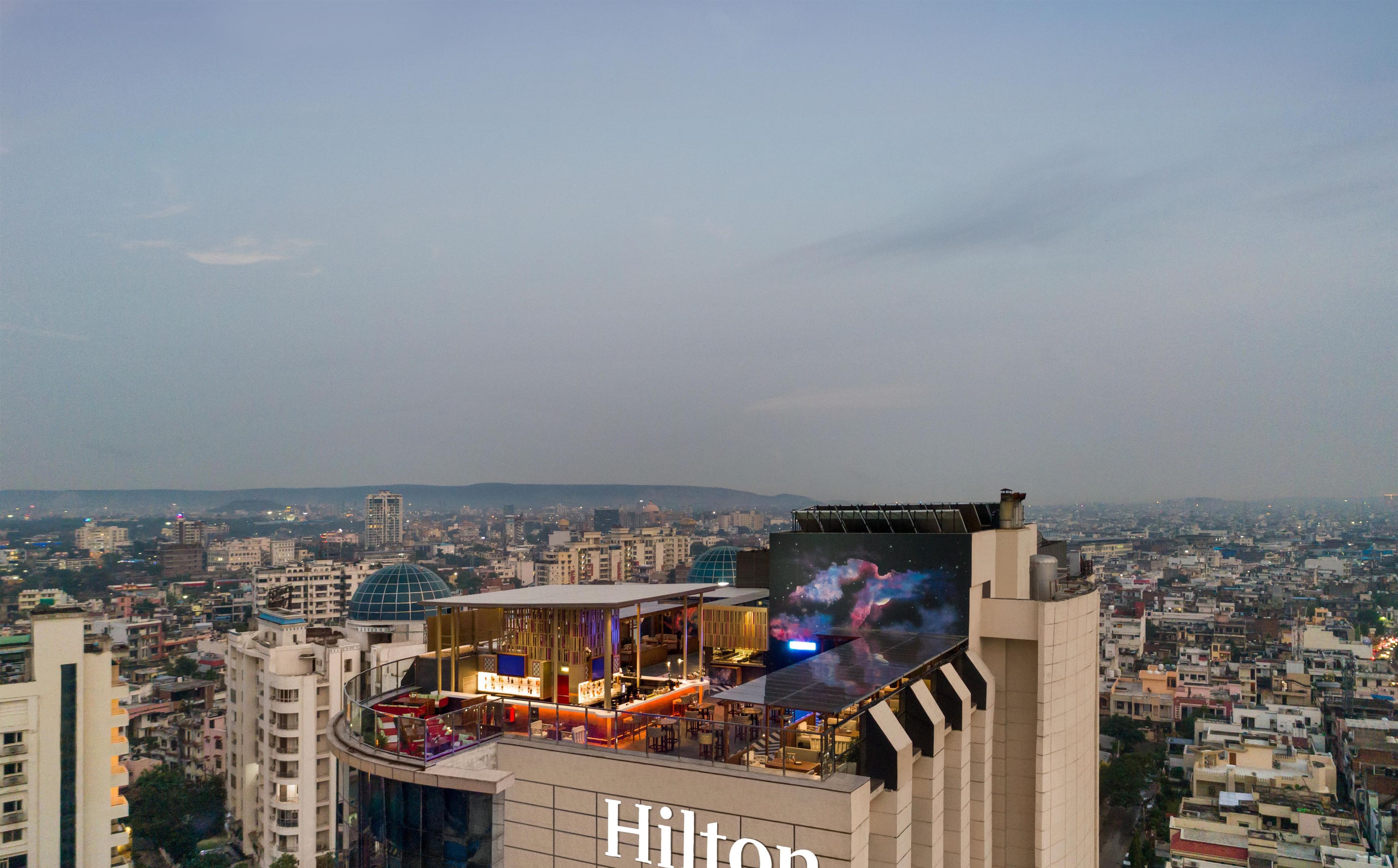Ett hotell med en bar på takterrassen, en stor glasfasad och utsikt över stadsbilden.