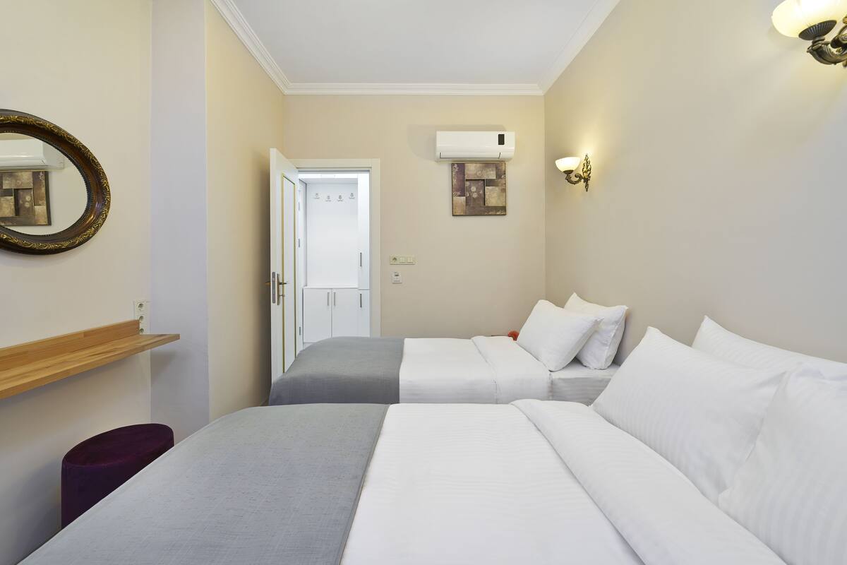 A hotel room with two beds, a wooden shelf, a mirror, an air conditioning unit, and a door leading to another room.