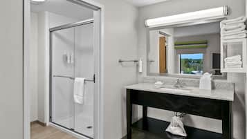 A modern bathroom with a glass shower door, a vanity with a black countertop, and a mirror above the sink.