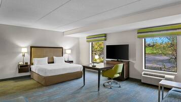 Habitación de hotel con cama, escritorio, televisor y ventanas amplias.