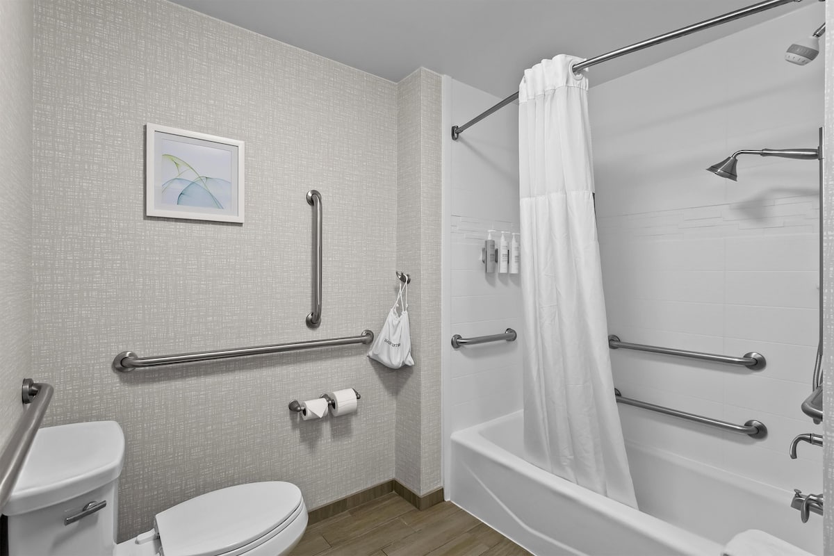 A bathroom with a toilet, bidet, and bathtub. It includes grab bars and a shower curtain.