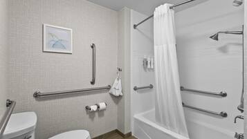 Un baño con inodoro, bidé y bañera. Incluye barras de apoyo y cortina de ducha.