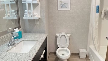 A bathroom with a sink, mirror, toilet, and shower.