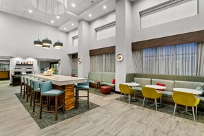 A modern hotel lobby with a bar area, seating arrangements, and a large window with curtains. - Hampton Inn & Suites Baltimore/Woodlawn (Windsor Mill)