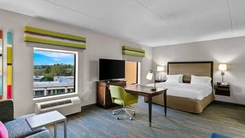 Habitación de hotel con cama, escritorio, silla, televisión y vistas de la ciudad.