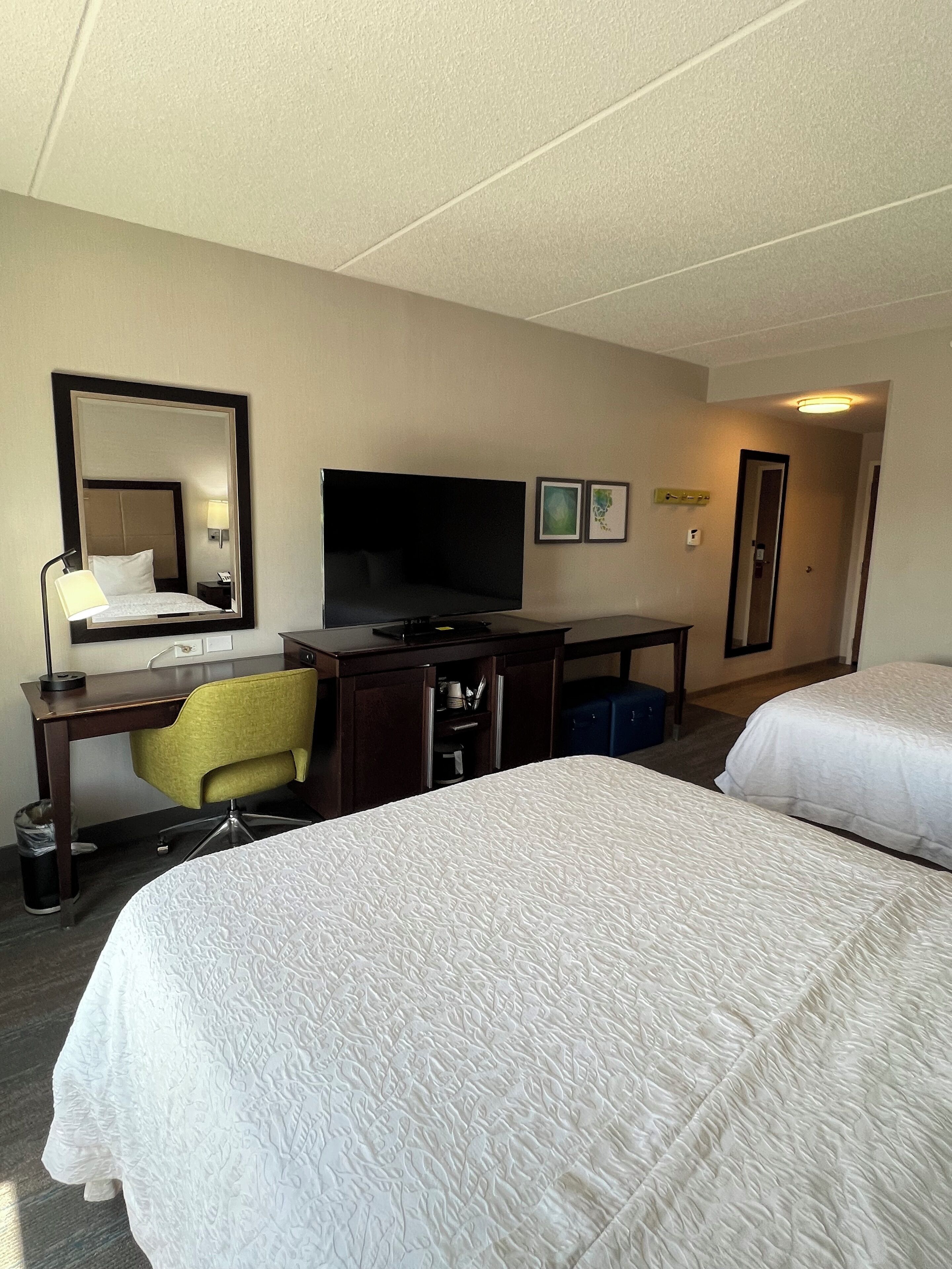 Una habitación de hotel con una cama, un escritorio con silla, un televisor y un espejo.