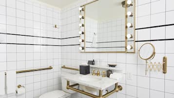 A bathroom with white subway tiles, a gold-framed mirror with lights, a round mirror, a marble sink, and a toilet.