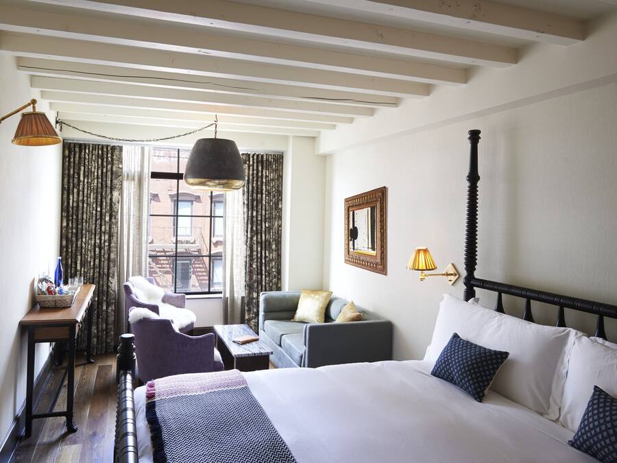 A hotel room with a bed, a desk, a chair, a sofa, and a window with curtains.