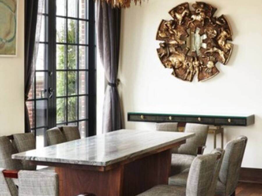 A dining area with a large table, chairs, a chandelier, and a decorative wall piece.