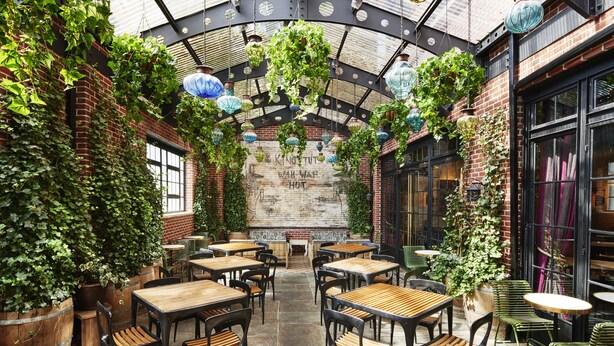 Un patio interior con paredes de ladrillo, faroles colgantes y mesas y sillas para comer.