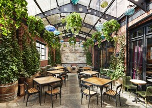 An indoor patio area with brick walls, hanging lanterns, and tables and chairs for dining. - The Ludlow Hotel (New York)