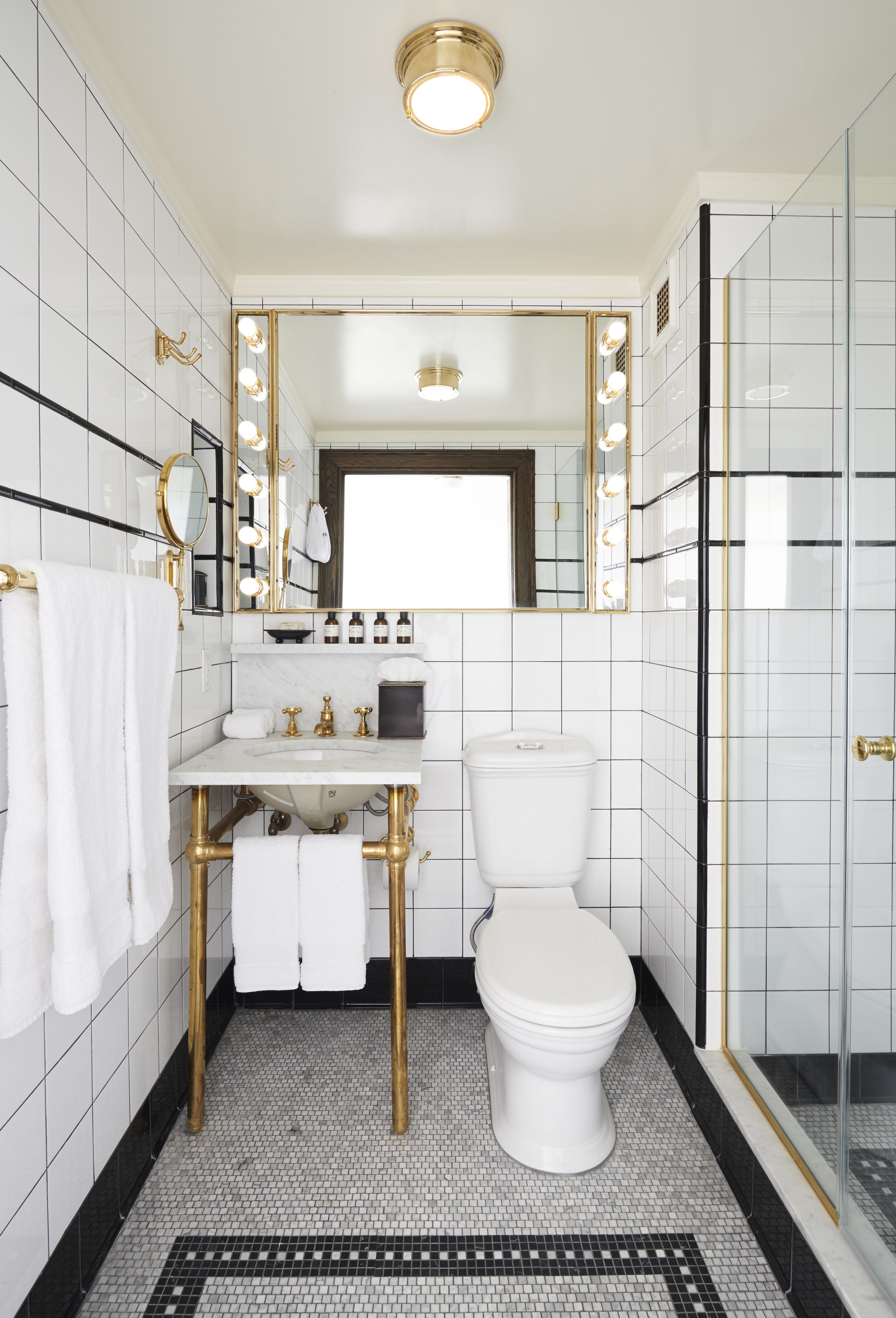 A bathroom with a white sink, gold fixtures, a white toilet, and a glass shower enclosure.