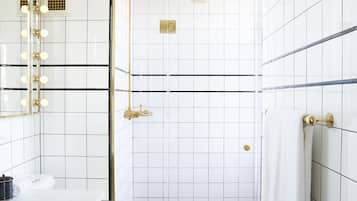 Ein Badezimmer mit weißen Fliesenwänden, einem goldfarbenen Duschkopf und einer weißen Toilette.