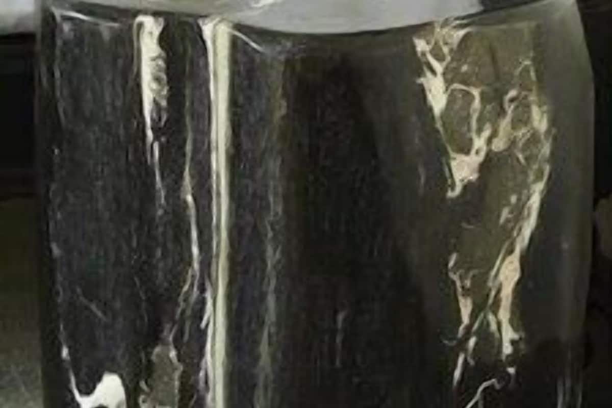 Una mesa redonda de color oscuro y acabado brillante, ubicada en una habitación con una silla blanca y un sofá oscuro.