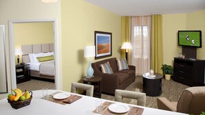 Habitación de hotel con comedor, sofá, televisor y ventana con cortinas.