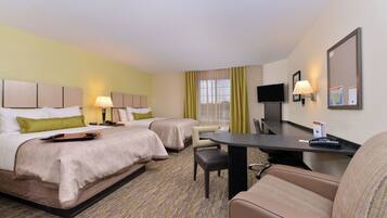 A hotel room with two beds, a desk, a chair, a television, and a bulletin board.