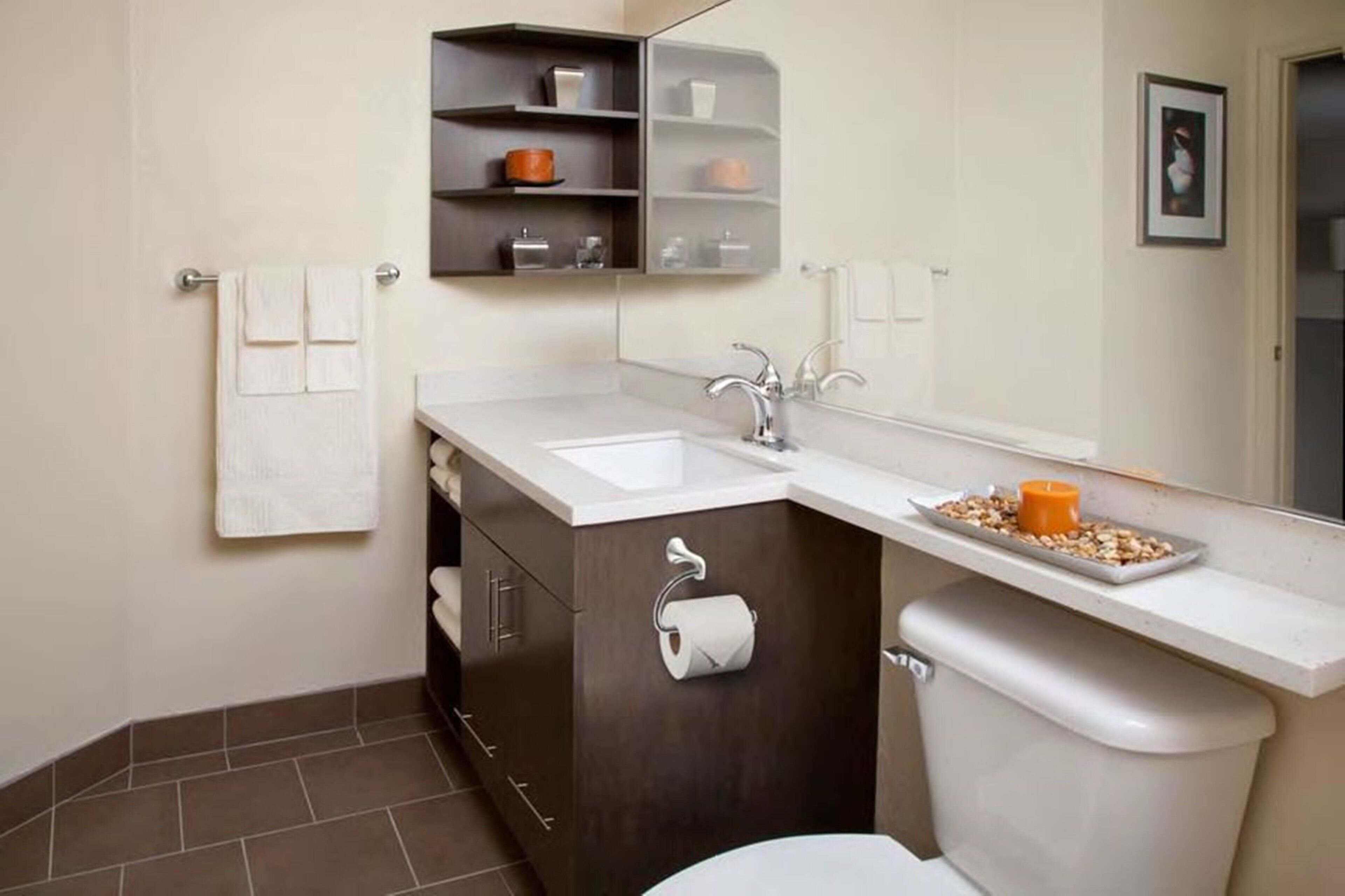 A modern bathroom with a white toilet, a sink, and a mirror. There is a shelf above the sink with a few items on it.