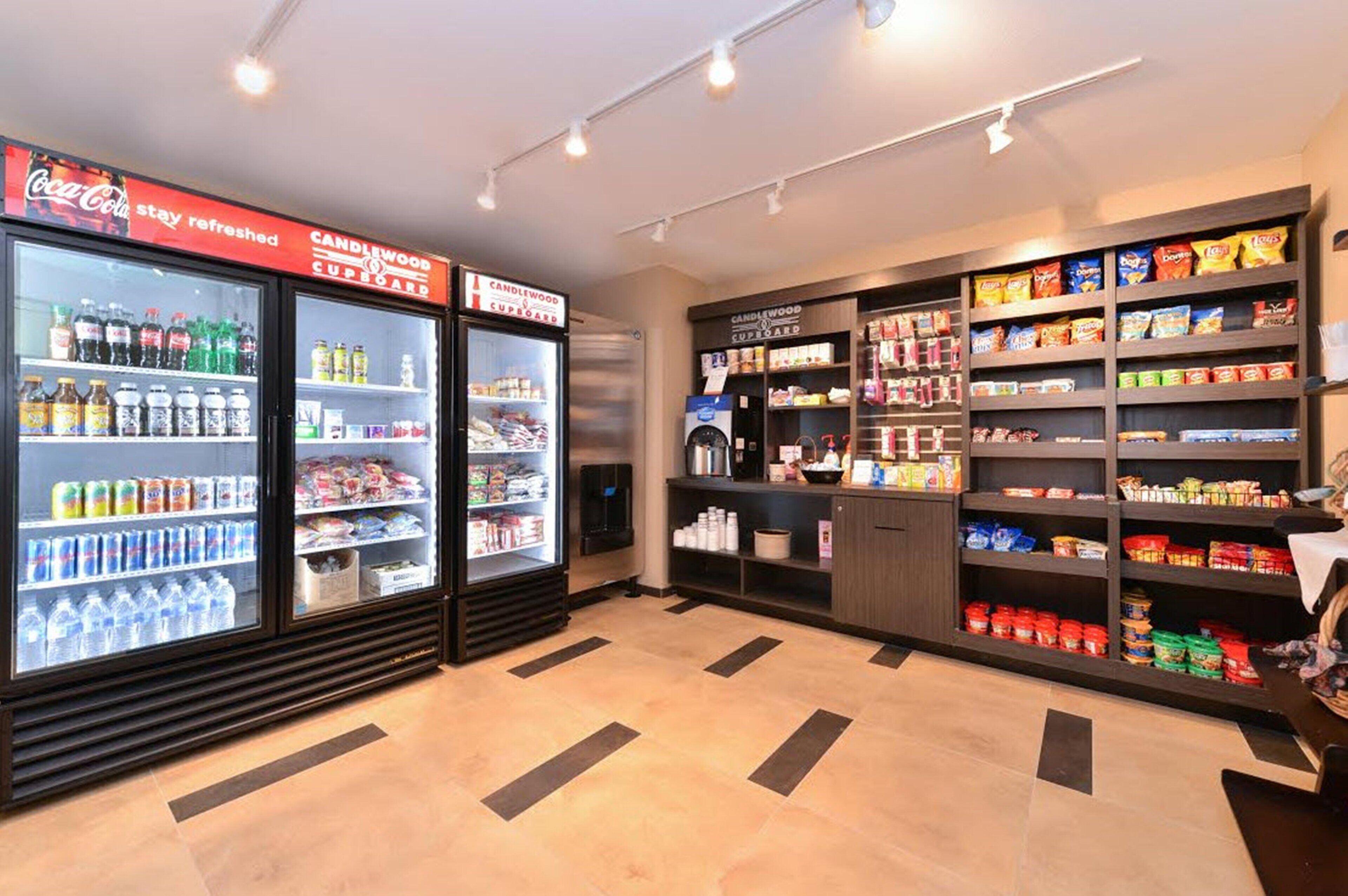 A self-service beverage area with refrigerated drink dispensers and shelves stocked with snacks and other items.