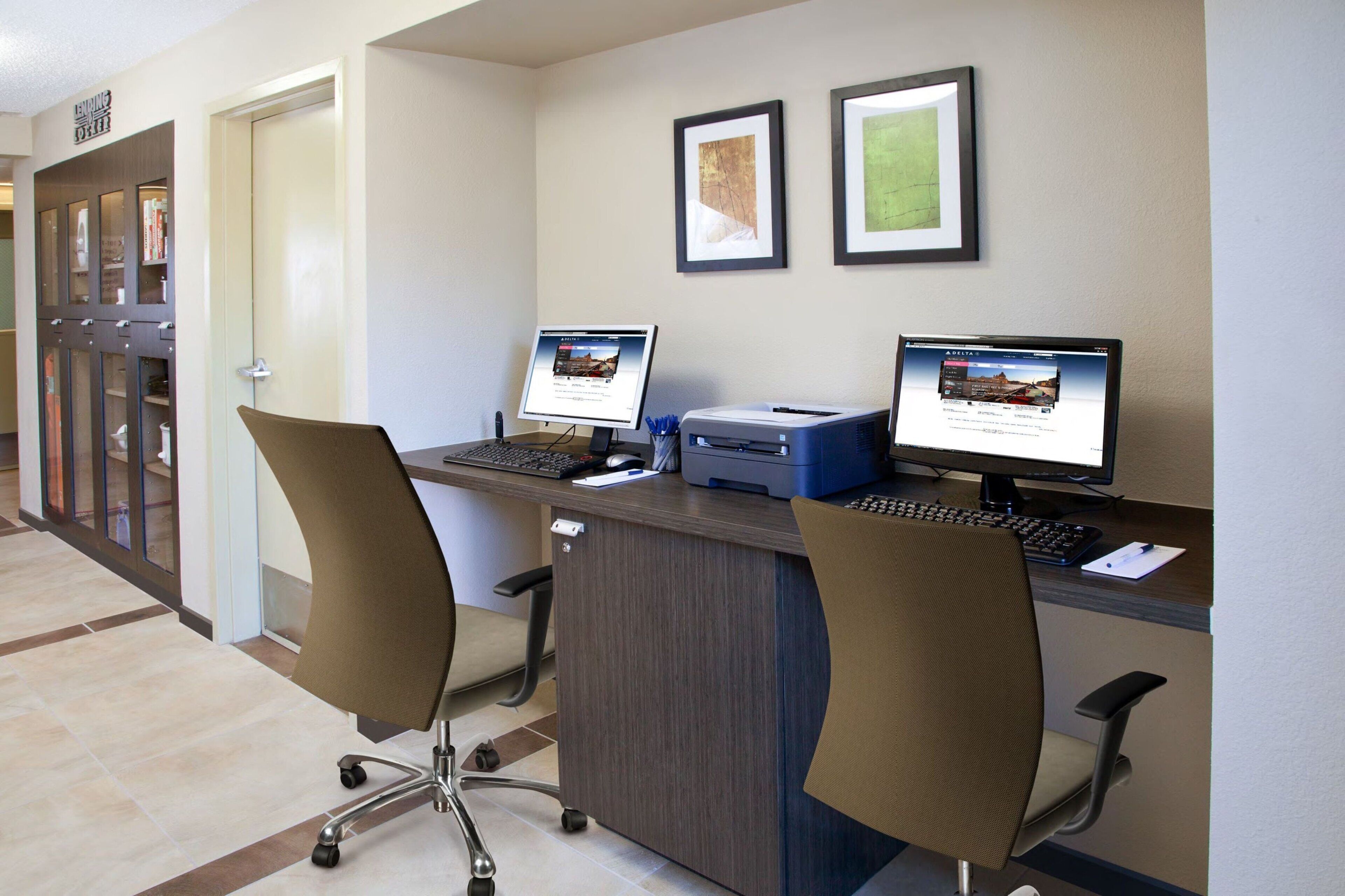 A hotel reception area with two computer workstations, a printer, and a desk lamp.