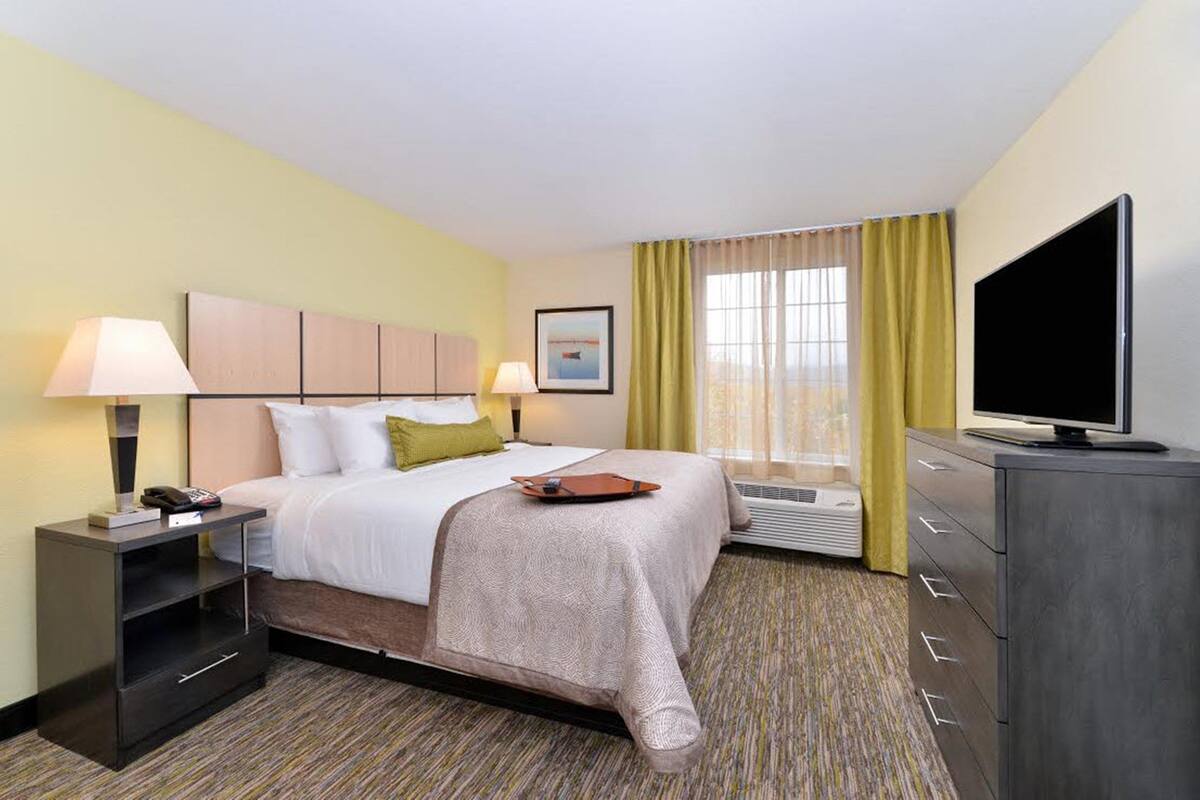 A hotel room with a bed, bedside tables, a TV, and a window with curtains.