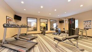 Un gimnasio con cintas de correr, máquinas de pesas y un espejo grande.