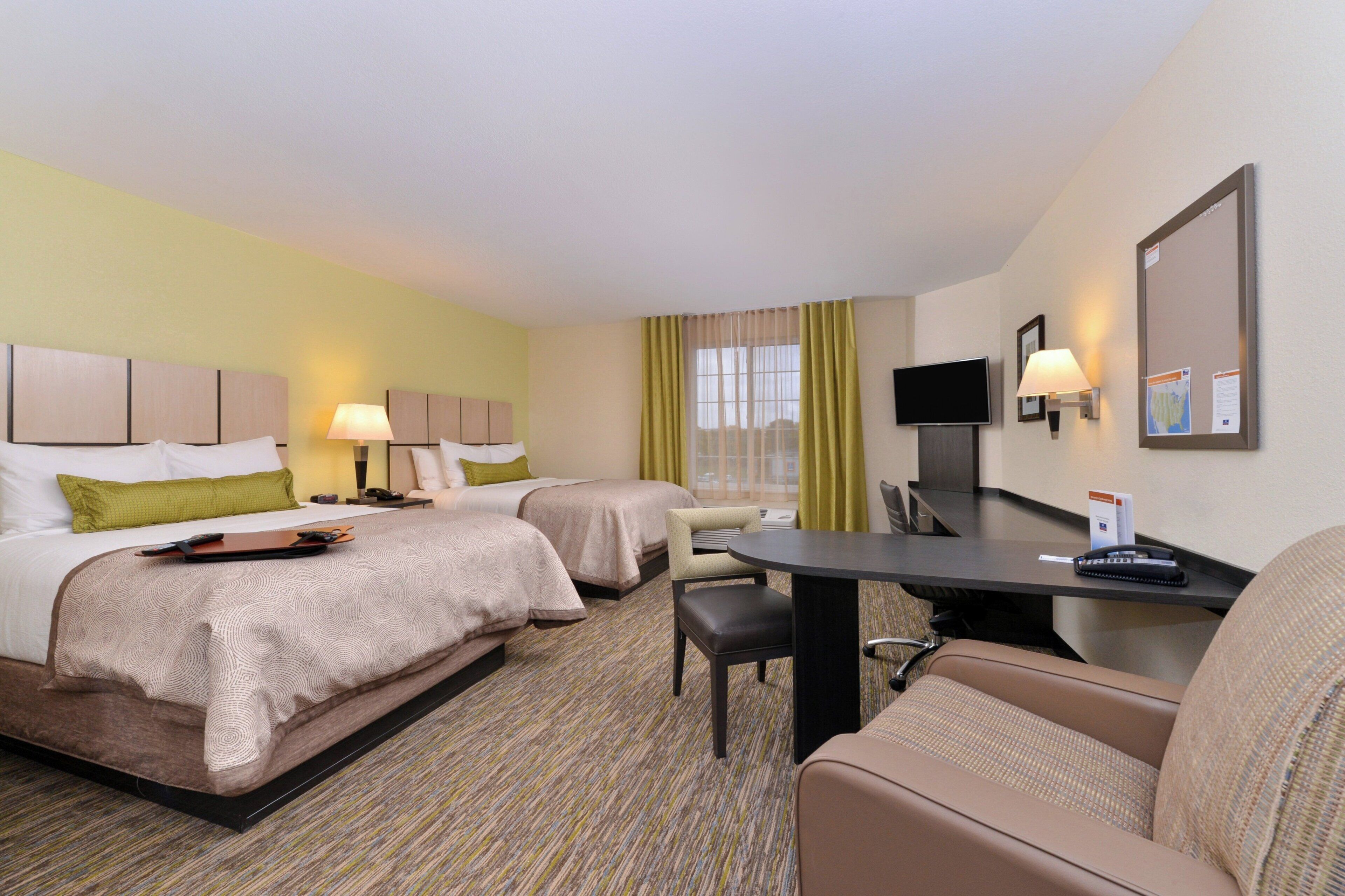 A hotel room with two beds, a desk, a chair, a television, and a window with curtains.