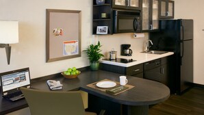 Cocina compacta con microondas, cafetera y lavabo. Hay un portátil sobre la mesa, un cuenco de fruta y una planta en maceta.