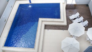 A swimming pool with a unique L-shaped design, surrounded by white lounge chairs and umbrellas. - Hotel Três Fronteiras (Foz do Iguaçu)