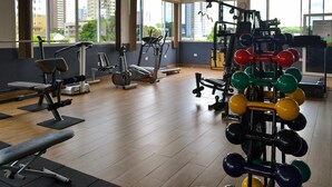 A gym with various exercise equipment, large windows, and a view of buildings outside. - Hotel Três Fronteiras (Foz do Iguaçu)