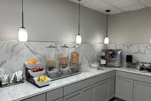 Une cuisine moderne dotée de plans de travail en marbre, d’un réfrigérateur et de différents distributeurs d’aliments.