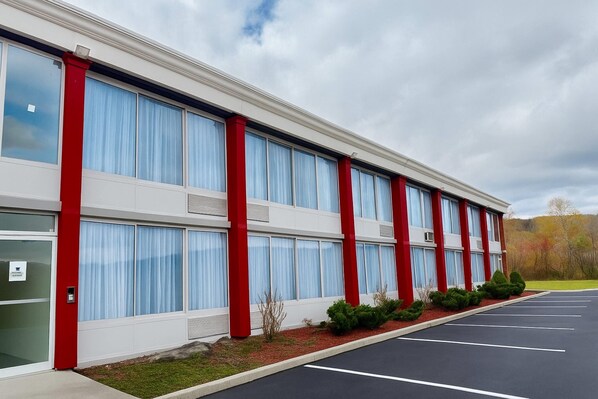 A modern building with large windows, red accents, and a parking lot. - Ramada by Wyndham Cobleskill (Cobleskill)