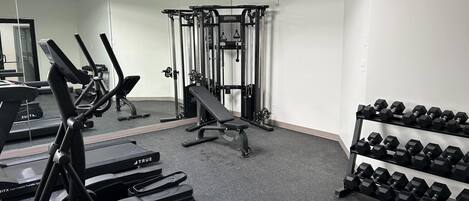 Ein Fitnessraum mit Laufbändern, einer Bank, einem Squat-Gestell und Kurzhanteln.