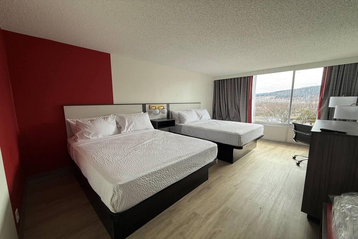 Ett hotellrum med två sängar, ett skrivbord, en stol och ett stort fönster med utsikt.
