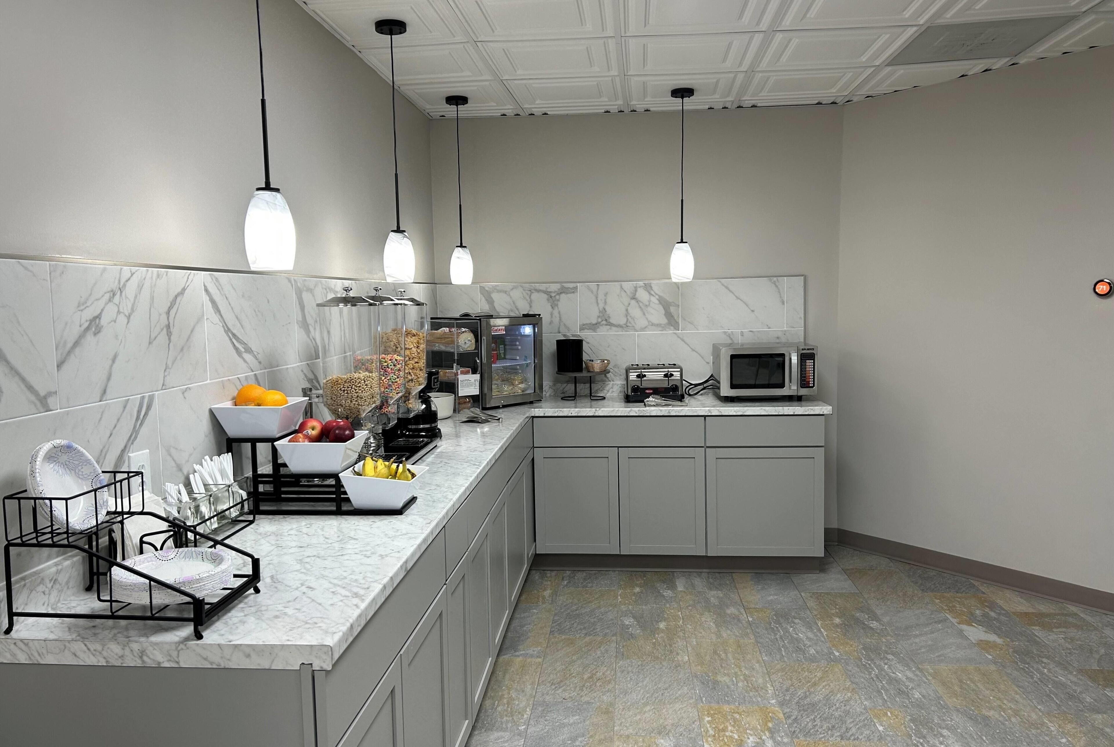 Une cuisine moderne dotée de plans de travail en marbre, d’un four à micro-ondes encastré et de luminaires suspendus.