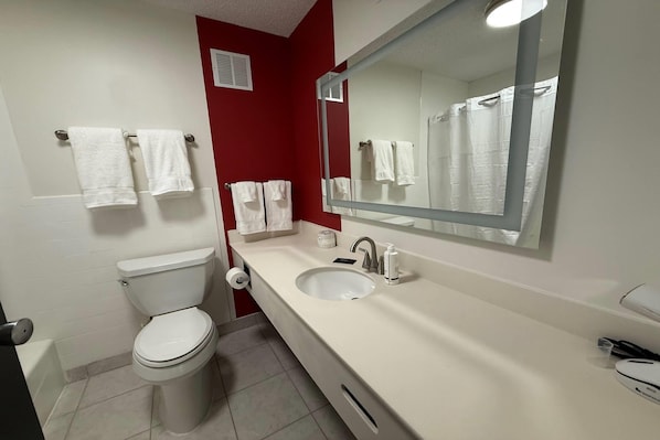 A bathroom with a toilet, sink, mirror, and towels. - Ramada by Wyndham Cobleskill (Cobleskill)