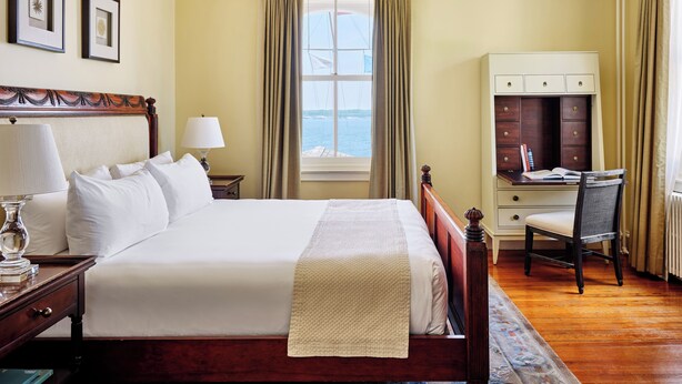 A hotel room with a large bed, a desk, a chair, a nightstand, and a window with curtains. - Castle Hill Inn (Newport)