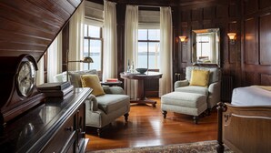 A traditional room with wooden paneling, two armchairs, a round table, a clock, and a large mirror. - Castle Hill Inn (Newport)